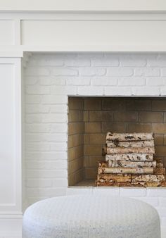 a fireplace with logs stacked on top of it and a stool in front of it