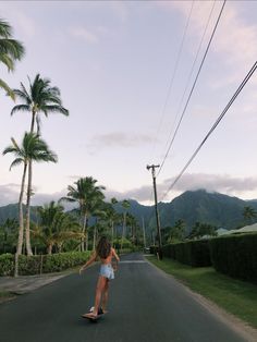 a woman riding a skateboard down the middle of a road next to palm trees