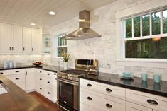 a kitchen with white cabinets and black counter tops, stainless steel oven hood over the stove