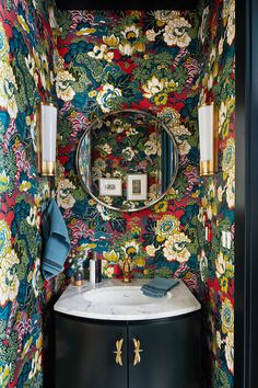 a bathroom with colorful wallpaper and a round mirror above the sink in front of it