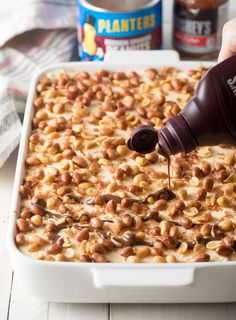 someone pouring peanut butter on top of a casserole in a baking dish with other ingredients nearby