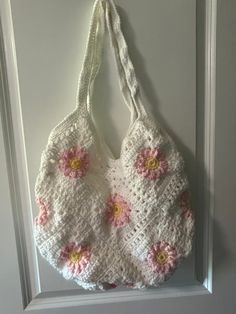 a crocheted bag hanging on the wall with pink and yellow flowers in it