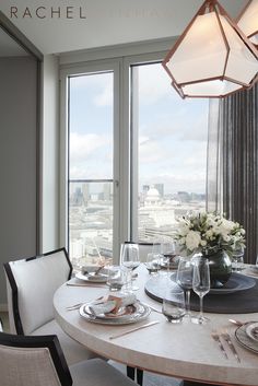 a dining room table with plates and glasses on it in front of large windows overlooking the city