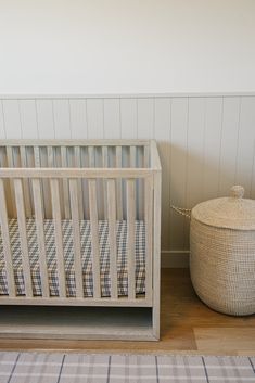 a baby crib next to a basket on the floor in a room with white walls