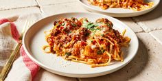 two plates of pasta with meat and sauce on them, next to a fork and knife