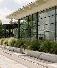 an outdoor seating area with large windows and green plants on the side of the building