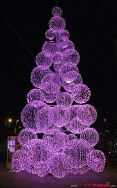 a purple christmas tree is lit up at night with balls all over it and lights in the shape of circles