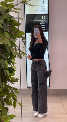 a woman taking a selfie with her cell phone in front of a plant and mirror