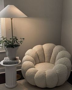 a white chair sitting next to a table with a lamp on it and a potted plant in the corner