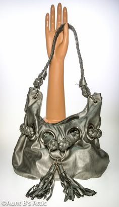 "80's to the Max!, vintage Bay Studio silver faux leather bucket style bag. Large silver metal rings hold the 18\" long braided handle. Another braided strap is woven through large silver metal rings in the front, and accented with 2 large tassels. The bag is lined with a leopard print cloth lining, and has 1 zippered pocket, and one open pocket. Snap strap closure. Bag sits on an oval base thats 7 1/2\" x 4 1/2\". Total height including strap-12\" Bag is in very good condition, and clean. *All Silver Bucket Bag With Silver-tone Hardware, Silver Bucket Bag With Silver-tone Hardware For Everyday Use, Silver Hobo Bag With Silver-tone Hardware Tote, Silver Hobo Bag With Silver-tone Hardware, Silver Leather Shoulder Bag With Hardware, Silver Shoulder Bag With Hardware For Everyday Use, Silver Tote Shoulder Bag With Metal Hardware, Silver Leather Shoulder Bag As Fashion Accessory, Large Tassels