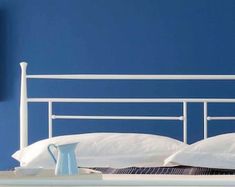 a bed with white sheets and pillows against a blue wall, next to a clock