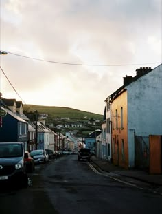 an empty street with cars parked on both sides and houses in the background at sunset