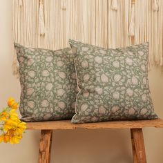 two pillows sitting on top of a wooden table next to a vase with yellow flowers