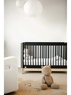 a teddy bear sitting on the floor in front of a crib with white walls