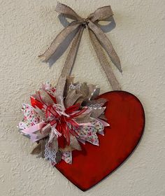 a red heart hanging on the wall with a bow and ribbon around it's center