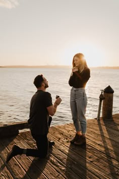 a man kneeling down next to a woman on top of a wooden pier near the ocean