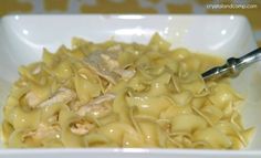 a white bowl filled with noodles and chicken in gravy next to a spoon