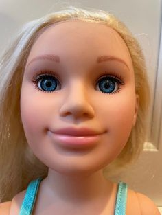 a close up of a doll with blonde hair and blue eyes looking at the camera