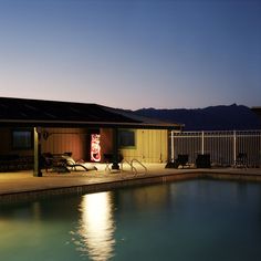 a pool at night with the lights on and chairs by it's edge lit up