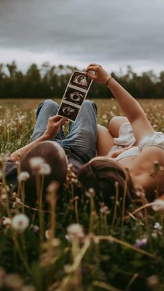 a woman laying in the grass holding up a cell phone with two buttons on it