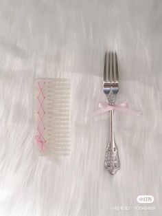 two forks and a comb are on a white fur covered surface with pink ribbon around it