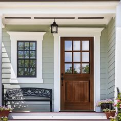 the front door of a house with potted plants on the steps and bench in front