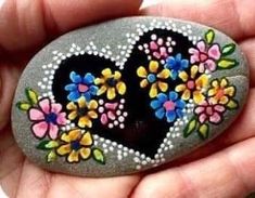 a hand holding a rock with flowers painted on it in the shape of a heart