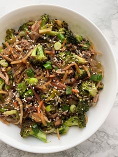 a white bowl filled with broccoli and sesame seed sprinkles on top of a marble table