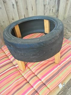 an old tire is sitting on top of a striped cushion in front of a wooden fence