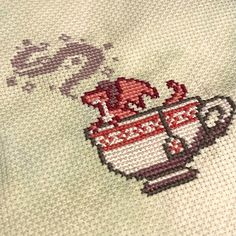 a close up of a cross - stitch pattern on a white cloth with a red cup