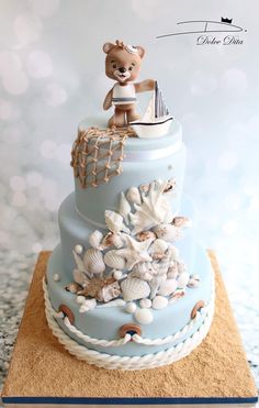 a teddy bear is sitting on top of a blue tiered cake with seashells