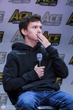 a young man sitting in front of a microphone with his hand to his mouth while talking into a microphone