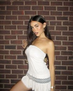 a young woman posing in front of a brick wall with her hand on her hip