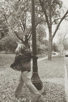 black and white photograph of woman walking on sidewalk next to lamp post