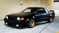 a black car with gold rims parked in a parking lot next to a concrete wall