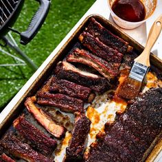 bbq ribs with barbecue sauce on the side and grilling utensils next to it