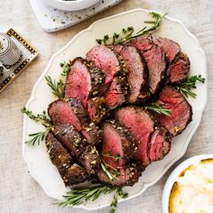 sliced steak with herbs on a plate next to dipping sauce