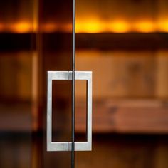 a square metal object hanging from a glass wall with lights in the background and wood flooring