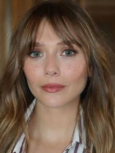 a close up of a person with long hair and blue eyes wearing a striped shirt