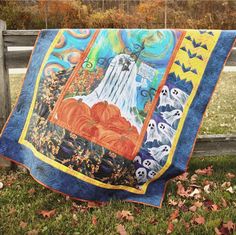 a quilt is hanging on a wooden fence in the grass with pumpkins and ghost decorations