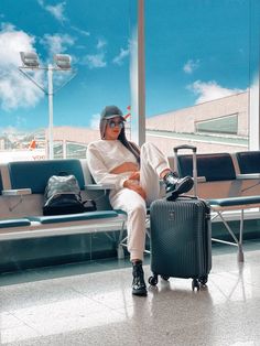 a woman sitting on top of a bench next to a luggage bag in an airport