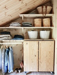 an attic closet with clothes and baskets on the top shelf, next to a wooden cabinet