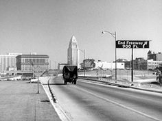 a black and white photo of an empty highway in the middle of town with tall buildings on either side