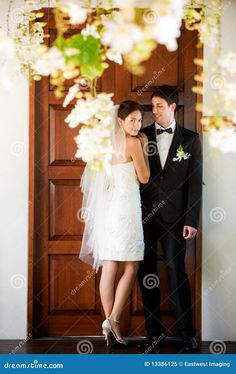 a bride and groom standing in front of a wooden door with white flowers on it