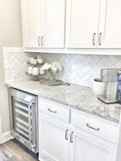 a kitchen with white cabinets and marble counter tops, an appliance in the corner