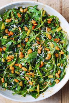 a white bowl filled with greens and nuts