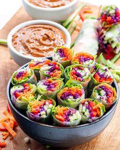 several different types of vegetable rolls on a cutting board with dipping sauces in the background