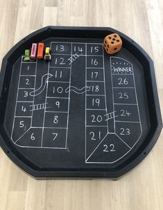 a chalk board game with dices and numbers on the side, sitting on a wooden floor