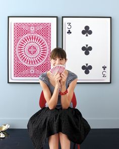 a woman sitting on a chair in front of two framed pictures and holding her hands together