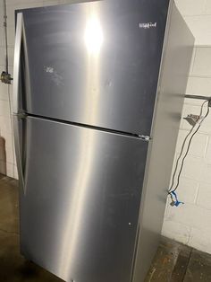 a metallic refrigerator sitting in a room next to a white brick wall with wires on it